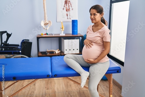 Fotografia Young latin woman pregnant patient sitting on massage table at clinic