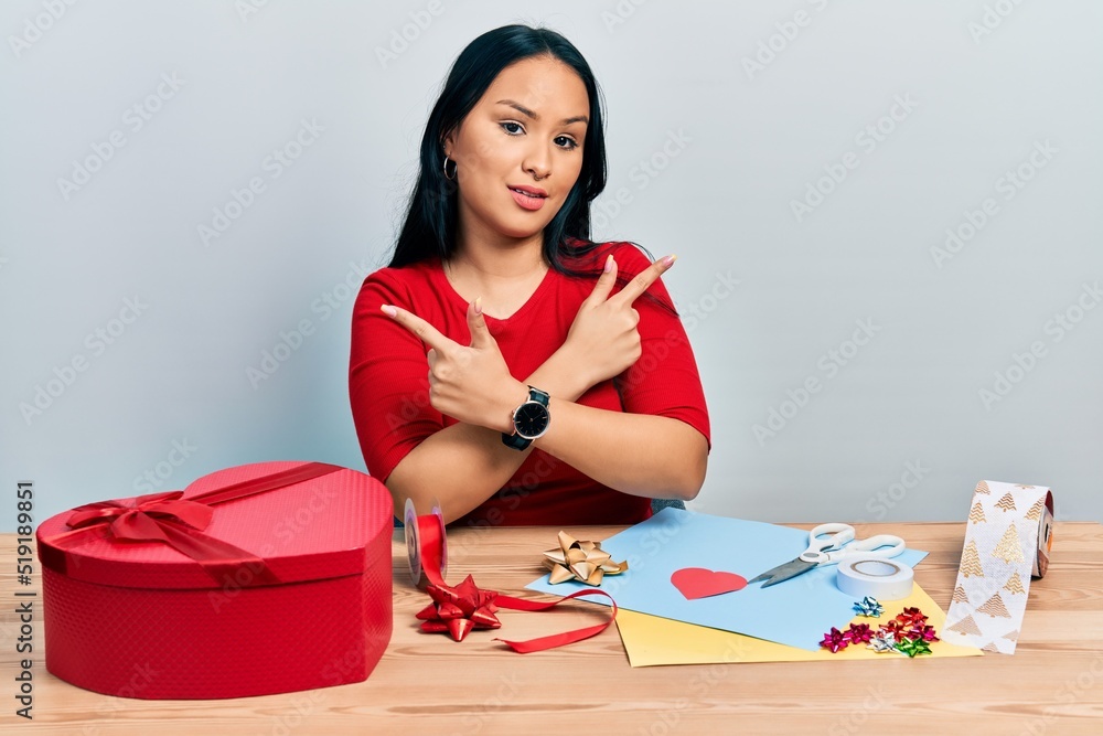 Beautiful hispanic woman with nose piercing doing handcraft creative decoration pointing to both sides with fingers, different direction disagree Beautiful hispanic woman with nose piercing doing handcraft creative decoration pointing to both sides with fingers, different direction disagree