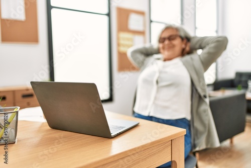 Middle age grey-haired businesswoman smiling happy relaxed with hands on head at the office.
