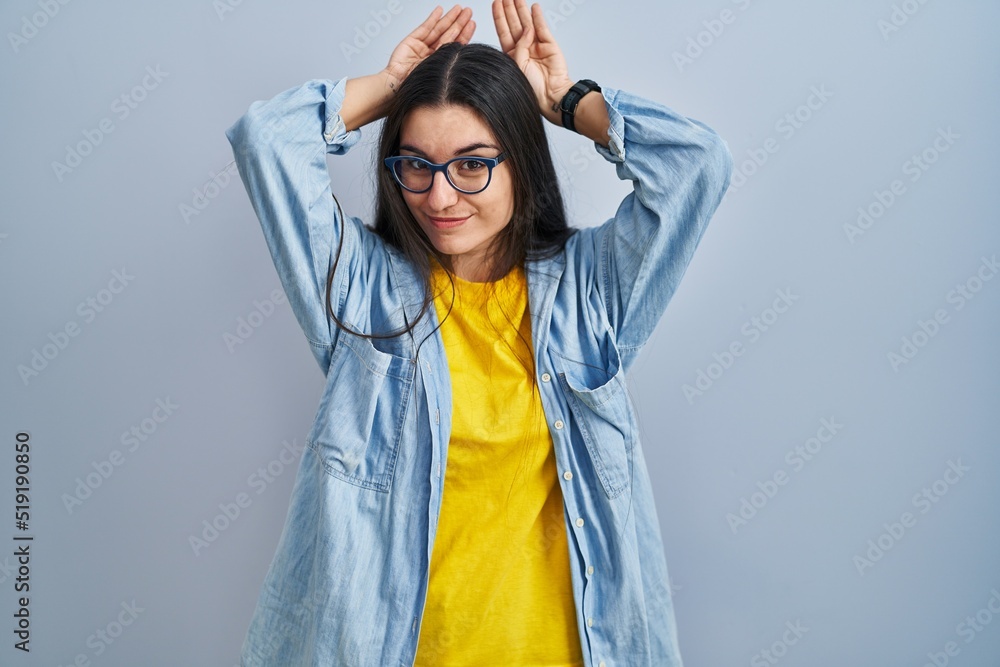 Young hispanic woman standing over blue background doing bunny ears gesture with hands palms looking cynical and skeptical. easter rabbit concept. Young hispanic woman standing over blue background doing bunny ears gesture with hands palms looking cynical and skeptical. easter rabbit concept.
