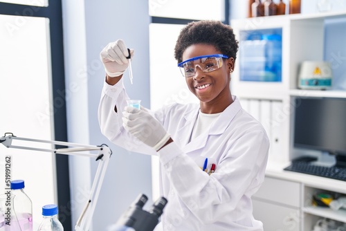 African american woman wearing scientist uniform measuring liquid at laboratory