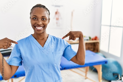 Black woman with braids working at pain recovery clinic looking confident with smile on face  pointing oneself with fingers proud and happy.