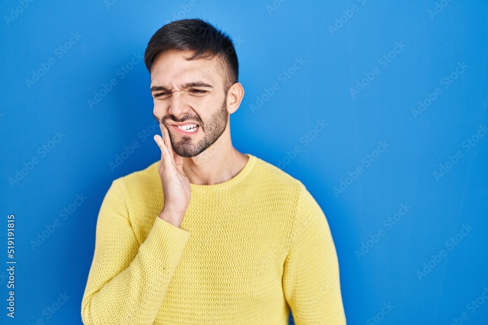 Hispanic man standing over blue background touching mouth with hand with painful expression because of toothache or dental illness on teeth. dentist Hispanic man standing over blue background touching mouth with hand with painful expression because of toothache or dental illness on teeth. dentist