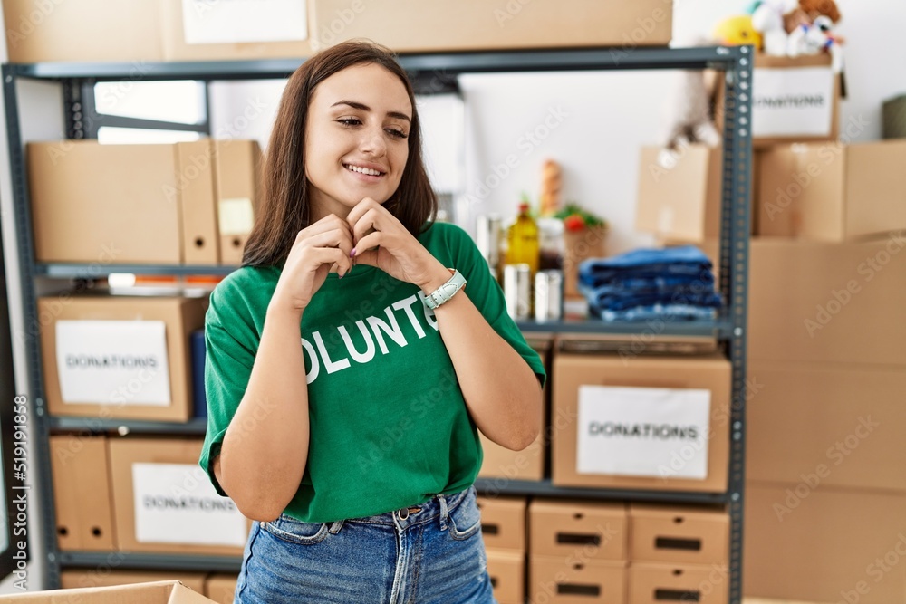 Young brunette woman wearing volunteer t shirt at donations stand laughing nervous and excited with hands on chin looking to the side Young brunette woman wearing volunteer t shirt at donations stand laughing nervous and excited with hands on chin looking to the side