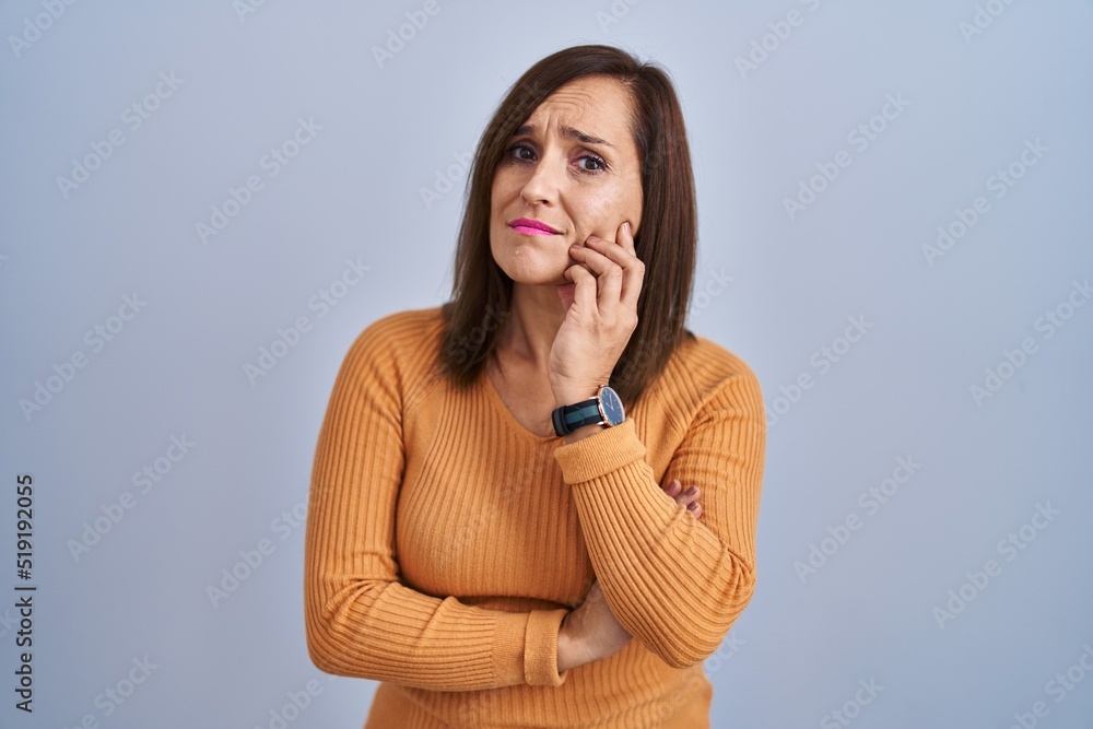 Middle age brunette woman standing wearing orange sweater with hand on chin thinking about question, pensive expression. smiling with thoughtful face. doubt concept. Middle age brunette woman standing wearing orange sweater with hand on chin thinking about question, pensive expression. smiling with thoughtful face. doubt concept.