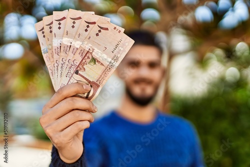 Young arab man smiling confident holding riyal banknotes at park photo