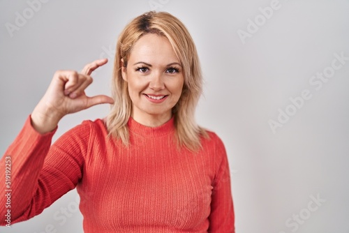 Blonde woman standing over isolated background smiling and confident gesturing with hand doing small size sign with fingers looking and the camera. measure concept. © Krakenimages.com