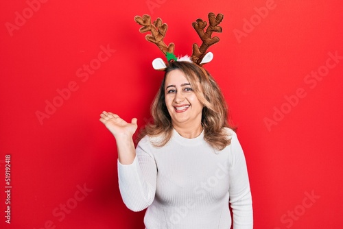 Fotobehang Middle age caucasian woman wearing cute christmas reindeer horns smiling cheerful presenting and pointing with palm of hand looking at the camera