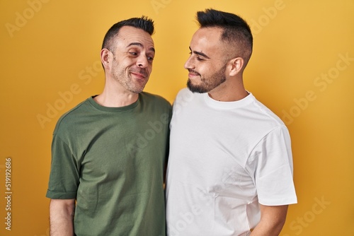 Homosexual couple standing over yellow background smiling looking to the side and staring away thinking.
