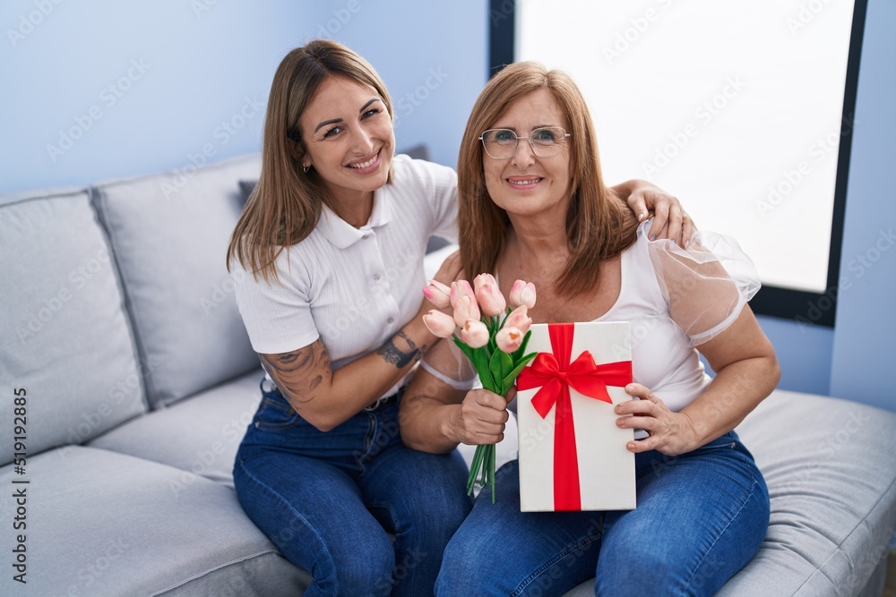 Mother and daughter surprise with gift and flowers hugging each other at home Mother and daughter surprise with gift and flowers hugging each other at home