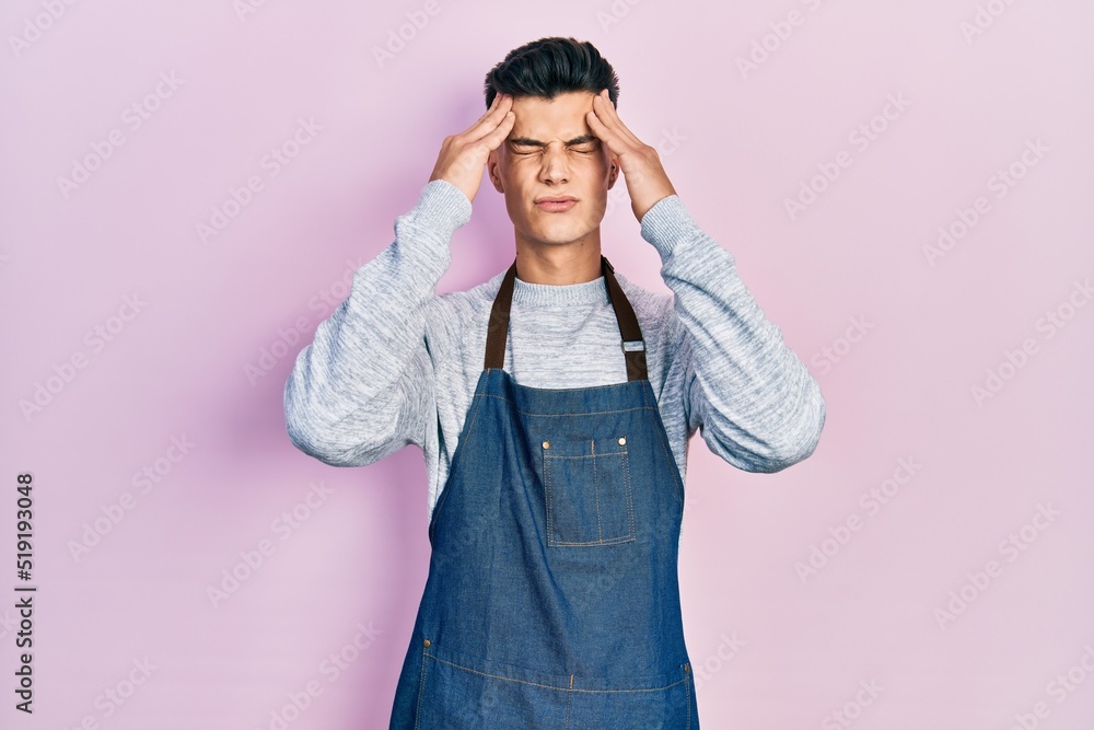 Young hispanic man wearing apron suffering from headache desperate and stressed because pain and migraine. hands on head. Young hispanic man wearing apron suffering from headache desperate and stressed because pain and migraine. hands on head.