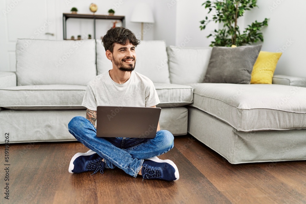Young hispanic man using laptop sitting on the floor at home.
