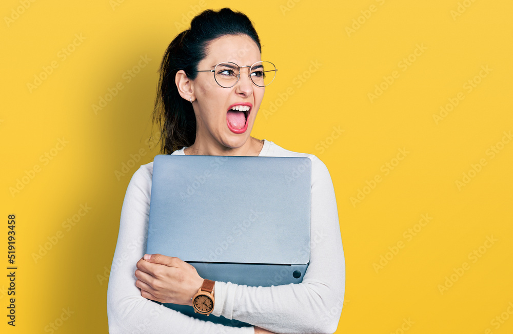 Young hispanic woman working using computer laptop angry and mad screaming frustrated and furious, shouting with anger. rage and aggressive concept. Young hispanic woman working using computer laptop angry and mad screaming frustrated and furious, shouting with anger. rage and aggressive concept.