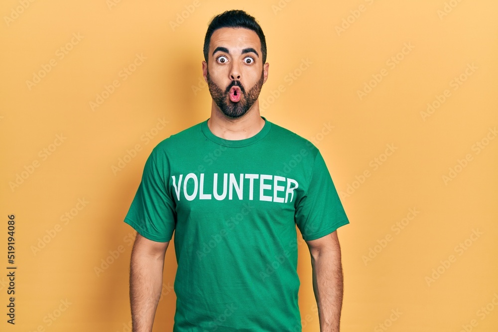 Handsome hispanic man with beard wearing volunteer t shirt scared and amazed with open mouth for surprise, disbelief face Handsome hispanic man with beard wearing volunteer t shirt scared and amazed with open mouth for surprise, disbelief face