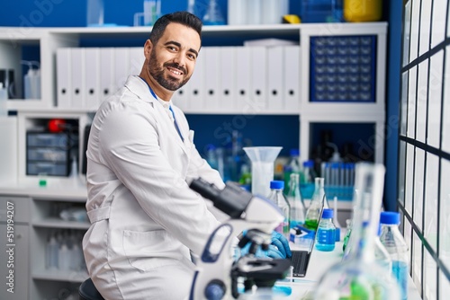 Young hispanic man scientist smiling confident using laptop at laboratory