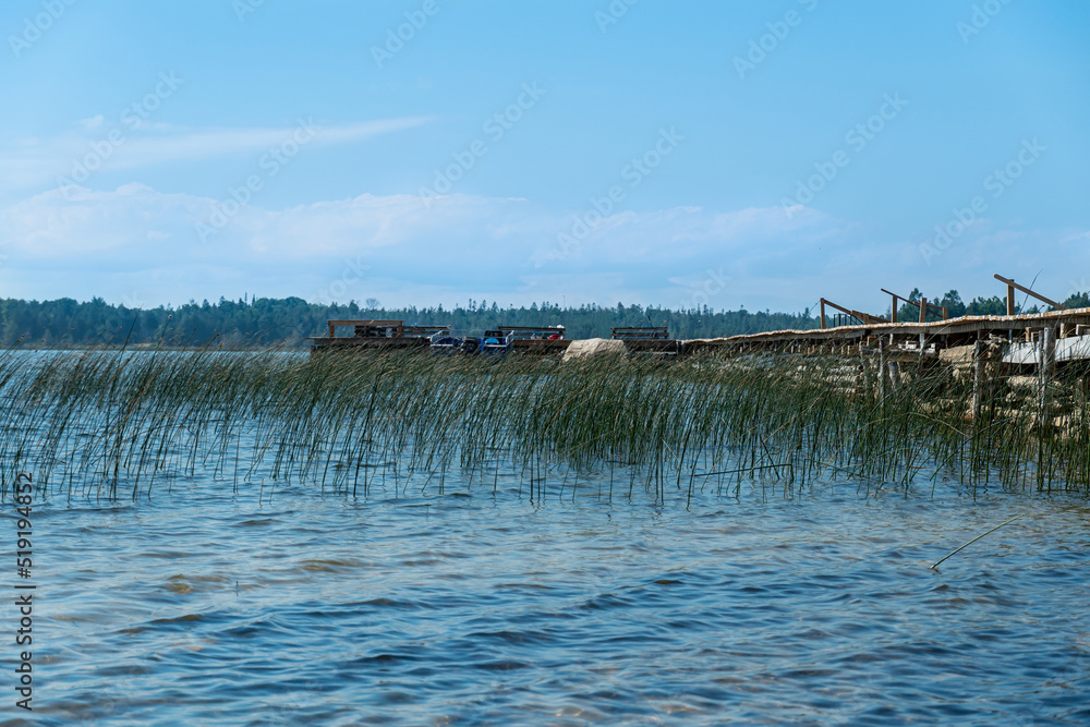 Old weathered wooden boat pier for fishing boats in Pike Bay water, lake Huron peninsula. Water grass and pine trees with cottages and cabins. Meditation and relaxation view panorama, Ontario Canada.