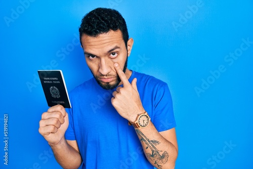 Hispanic man with beard holding italy passport pointing to the eye watching you gesture, suspicious expression