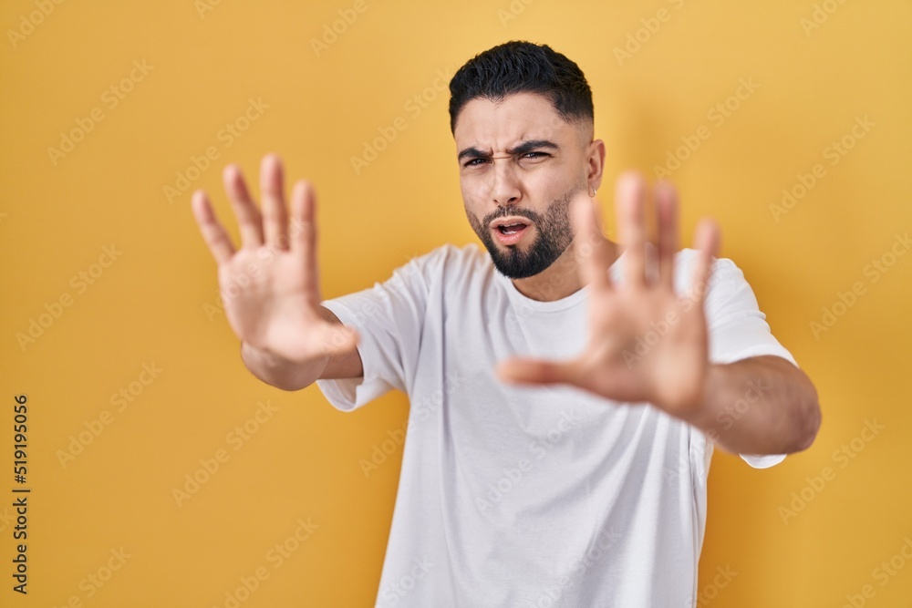 Young handsome man wearing casual t shirt over yellow background afraid and terrified with fear expression stop gesture with hands, shouting in shock. panic concept. Young handsome man wearing casual t shirt over yellow background afraid and terrified with fear expression stop gesture with hands, shouting in shock. panic concept.