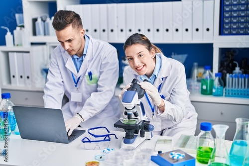 Man and woman scientists using laptop and microscope at laboratory