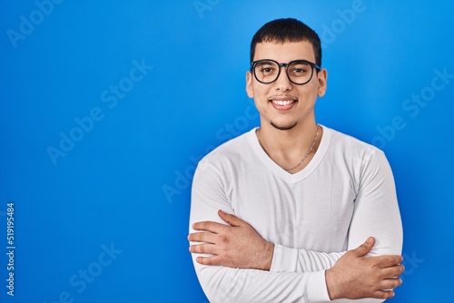 Young arab man wearing casual white shirt and glasses happy face smiling with crossed arms looking at the camera. positive person.