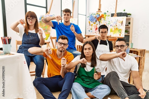 Group of people sitting at art studio with angry face, negative sign showing dislike with thumbs down, rejection concept