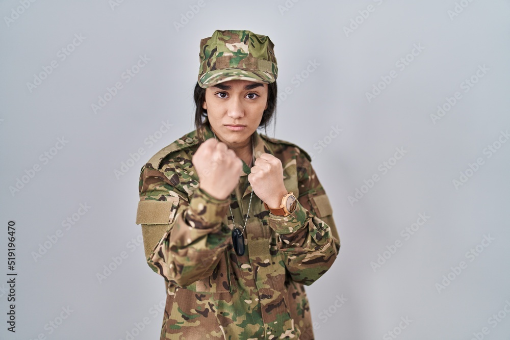Young south asian woman wearing camouflage army uniform ready to fight with fist defense gesture, angry and upset face, afraid of problem Young south asian woman wearing camouflage army uniform ready to fight with fist defense gesture, angry and upset face, afraid of problem