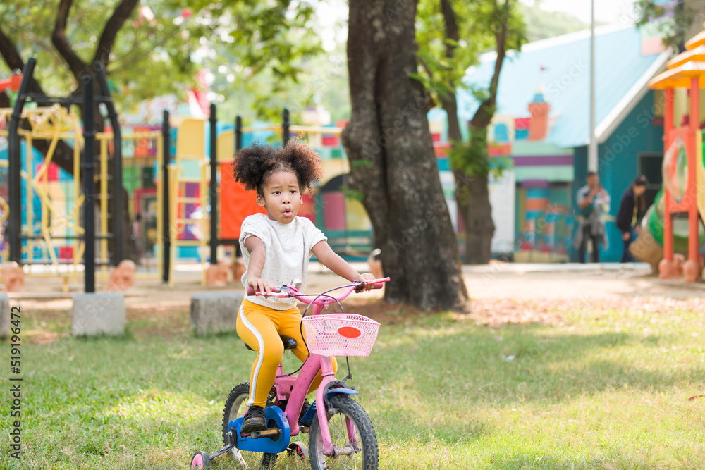 African American little girl playing and learning riding bicycle in the park. Sport outdoor, Happy on holiday, Field trip in garden African American little girl playing and learning riding bicycle in the park. Sport outdoor, Happy on holiday, Field trip in garden