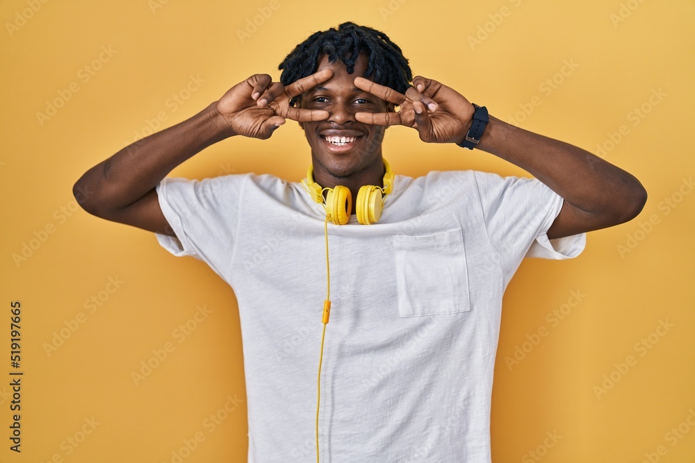 Young african man with dreadlocks standing over yellow background doing peace symbol with fingers over face, smiling cheerful showing victory Young african man with dreadlocks standing over yellow background doing peace symbol with fingers over face, smiling cheerful showing victory