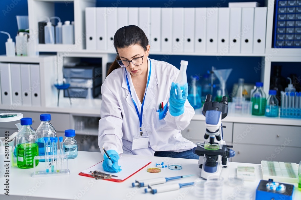 Young hispanic woman scientist write on document measuring liquid at laboratory Young hispanic woman scientist write on document measuring liquid at laboratory