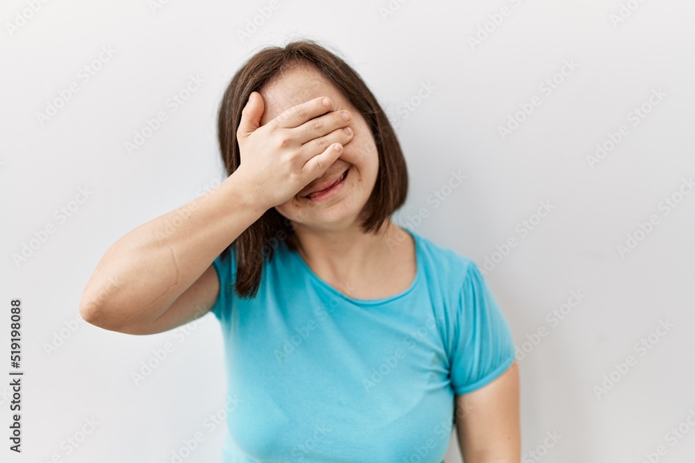 Young down syndrome woman standing over isolated background smiling and laughing with hand on face covering eyes for surprise. blind concept. Young down syndrome woman standing over isolated background smiling and laughing with hand on face covering eyes for surprise. blind concept.