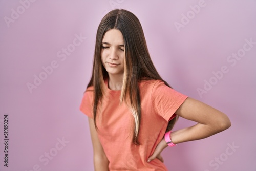 Teenager girl standing over pink background suffering of backache, touching back with hand, muscular pain