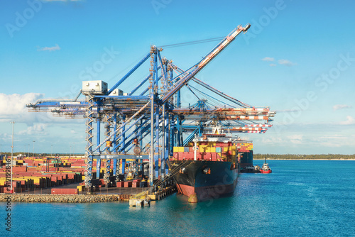 Port of Freeport Bahamas Container shipyard with heavy lifting Cranes and a ship coming in to dock assisted by tug boats