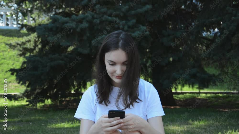 Beautiful young girl in the park with her phone in her hands chatting with friends on social networks