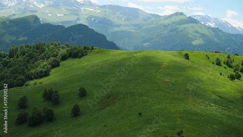 Alpine meadows with a hiking trail transition into snow-covered mountain peaks. White clouds in blue sky. Movement of the camera from bottom to top. Beautiful mountain scenery. Travel and tourism photo