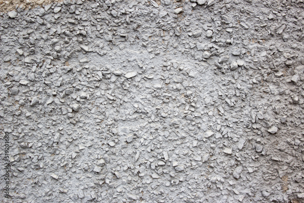 The texture of the concrete wall part with a small crumb of stone. Grey Textured cement wall background with a stone chip. Concrete wall of the building with stones of different sizes.