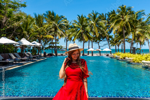 Travel vacation woman in red dress enjoying a summer vacation near swimming pool in tropical resort near the beach with sea view. Carefree girl tourist in hat relax in luxury resort, Thailand © TravelMedia