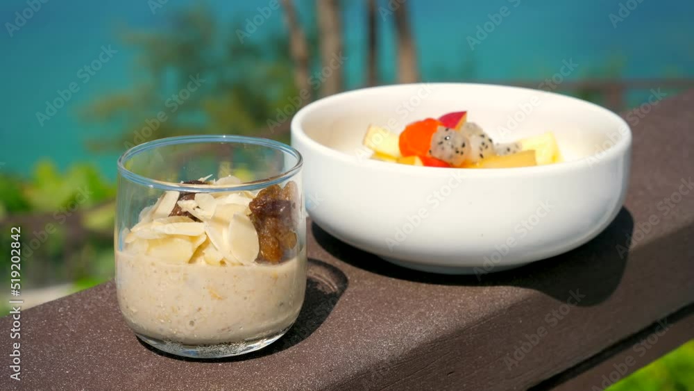 Healthy tropical breakfast with oatmeal and exotic fruits. Vacation in Thailand in modern resort with sea view on background. Vegan food, clean eating, diet or detox concept. Healthy tropical breakfast with oatmeal and exotic fruits. Vacation in Thailand in modern resort with sea view on background. Vegan food, clean eating, diet or detox concept.