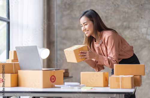 SME Online seller Young Asian woman working on laptop and box checking online order, check goods stock delivery package shipping postal. Asian woman startup SME small business at home office