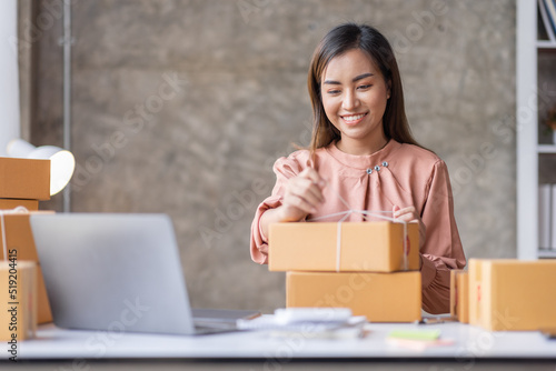 SME Online seller Young Asian woman working on laptop and box checking online order, check goods stock delivery package shipping postal. Asian woman startup SME small business at home office © David