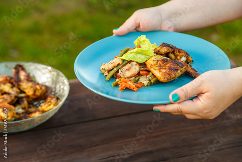Female hands put a plate with chicken and vegetables on the table next to a dish with grilled chicken.