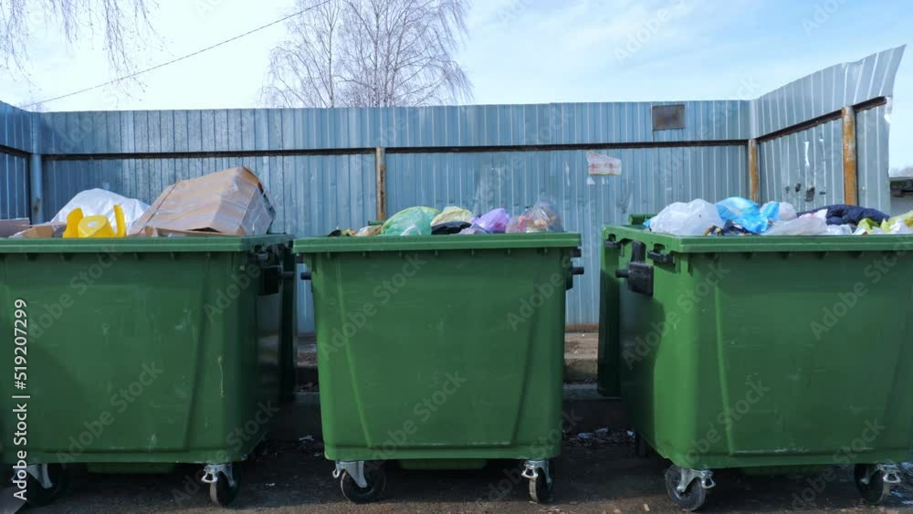 Large green containers full of rubbish in plastic bags located near metal barrier on sunny day on street. The concept of ecology and environmental protection. Large green containers full of rubbish in plastic bags located near metal barrier on sunny day on street. The concept of ecology and environmental protection.