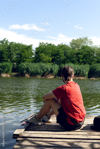 a man in a red T-shirt is resting in the summer near the lake looking at the calm water