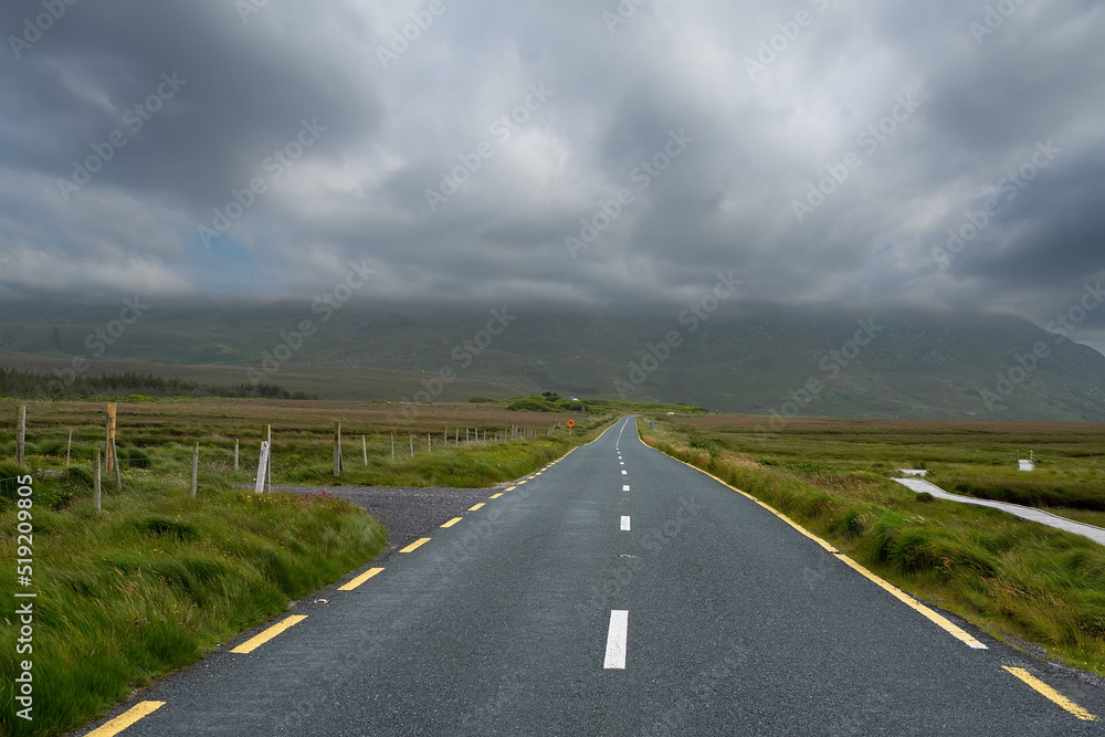 Small narrow road into mountains under low cloudy sky. Travel and transportation. West of Ireland.