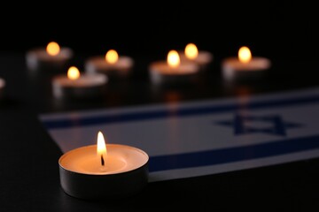 Burning candle and flag of Israel on black table. Holocaust memory day