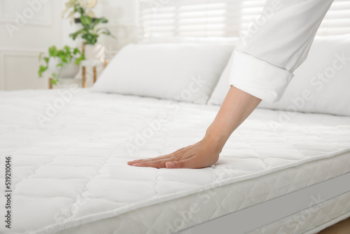 Woman touching soft white mattress on bed indoors, closeup