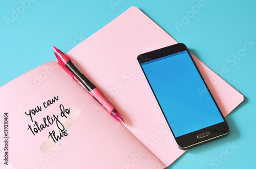 Smartphone and pink notebook with text You can do this on blue table. Mock up for design