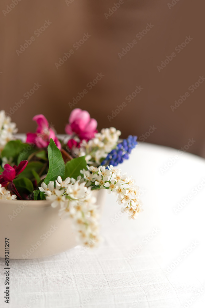 Summer blooming delicate flowers in a round vase on a table with a white tablecloth, a pastel bouquet and a delicate floral card