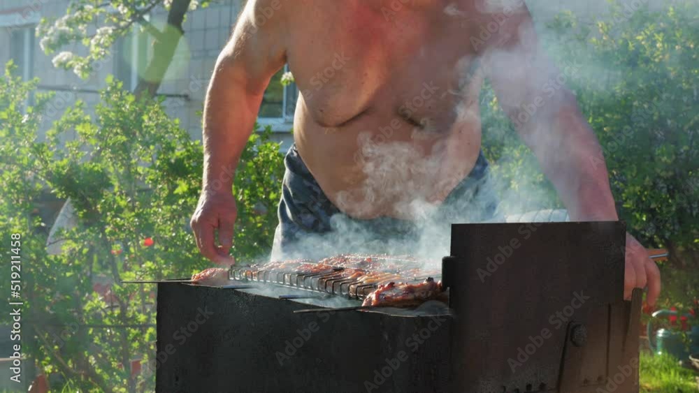 Fat funny man cooks kebabs and dances in the backyard. Unrecognizable man fries meat against the background of nature. The concept of gluttony and an idle lifestyle