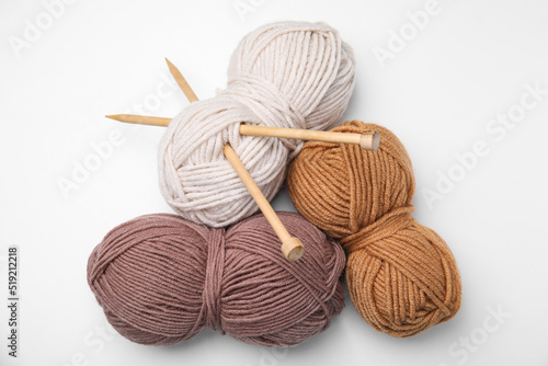 Soft woolen yarns and knitting needles on white background, top view