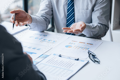 Two businessmen looking at sales data sheets in the office, they are business partners forming a startup company, are having a brainstorming meeting and planning an administration together.